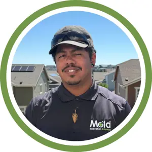 A man wearing a black cap and Mold Inspection Sciences shirt stands outside in front of houses on a sunny day, framed by a green and white circular border, ready to begin an assessment or testing as part of his investigation work.