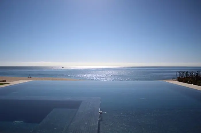 Infinity pool overlooking a calm, expansive ocean under a clear blue sky, with the horizon seamlessly blending between water and sky—a perfect setting for an inspection of serene beauty.