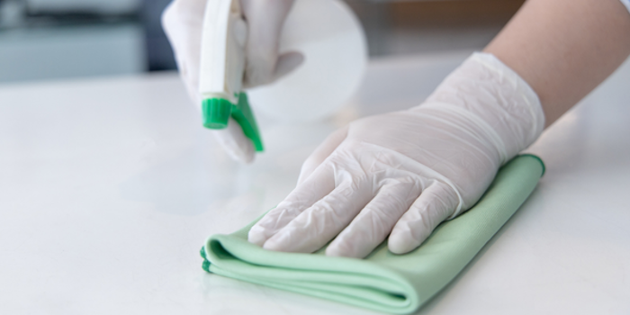 A person wearing white gloves diligently cleans a surface with a green cloth and spray bottle, ensuring no mold lingers after testing.