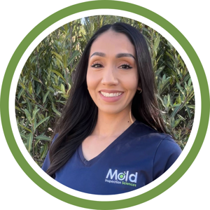 A woman with long dark hair smiles at the camera, wearing a dark blue shirt with the Mold Inspection Sciences logo. She stands in front of lush green foliage, framed by a circular green border, embodying expertise in mold testing and inspection.