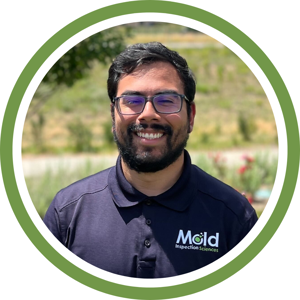 A man with glasses and a beard smiles outdoors, wearing a navy blue Mold Inspection Sciences polo shirt—highlighting his expertise in inspection and testing. The photo is framed by a green and white circular border.