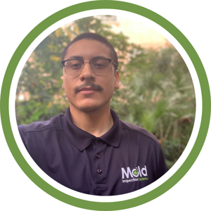 A person with glasses and a mustache, wearing a dark polo shirt featuring the Mold Inspection Sciences logo, stands outdoors against blurred greenery. Framed by a green ring, he appears ready for a thorough inspection.