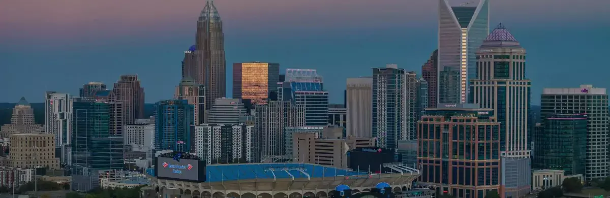 A skyline view of a city at dusk features a mix of modern skyscrapers with unique architectural designs. In the forefront, a large stadium stands proudly. The sky is a gradient of purple and blue, adding a serene backdrop to this urban sampling.