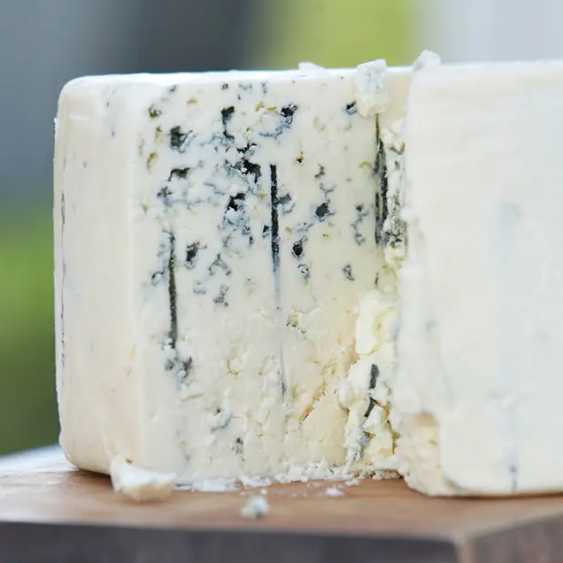 A close-up of a block of blue cheese on a wooden surface reveals its creamy texture and distinctive blue veins, inviting a thorough inspection to appreciate its complexity.