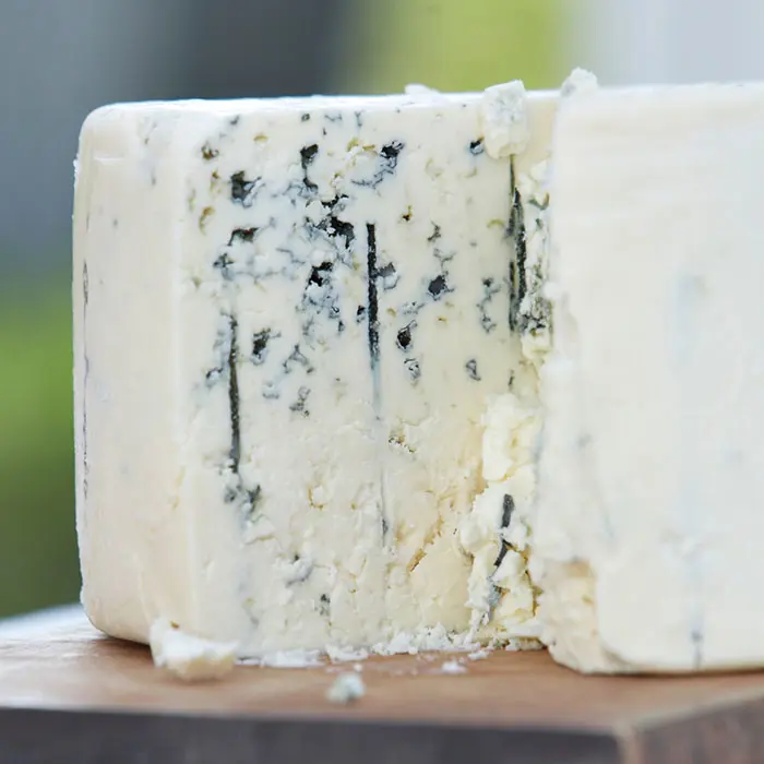 A close-up of a block of blue cheese on a wooden surface reveals its creamy texture and distinctive blue veins, inviting a thorough inspection to appreciate its complexity.