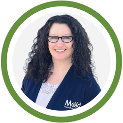 A woman with long curly hair and glasses smiles warmly, her dark blazer subtly featuring "Mold Assessment." The image is elegantly framed within a green circle.