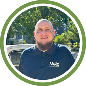 A person with facial tattoos and large earrings, wearing a polo shirt featuring the Mold Inspection Sciences logo, stands outdoors conducting sampling in front of a car and trees. The image is framed in a green-bordered circle.