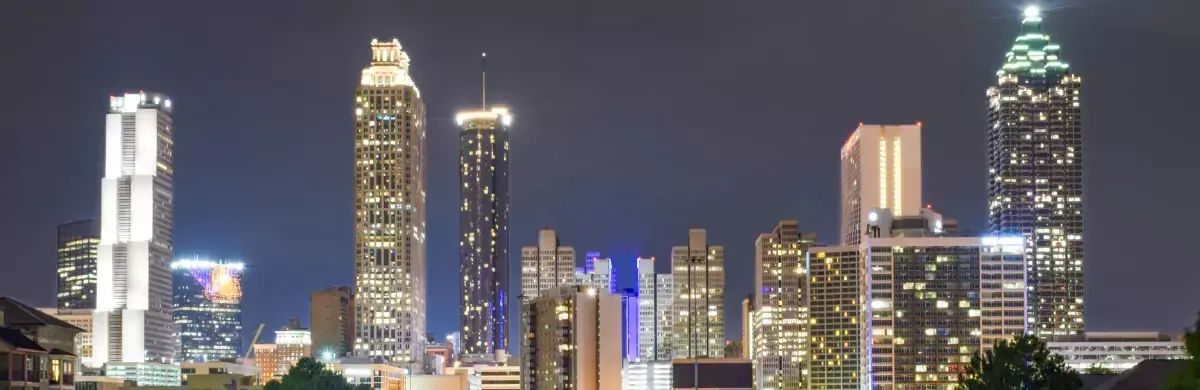 A nighttime city skyline featuring tall skyscrapers with illuminated windows against a dark sky evokes an urban atmosphere ripe for exploration. The buildings, each displaying various architectural styles, seem to set the stage for a metropolitan investigation into life after dark.