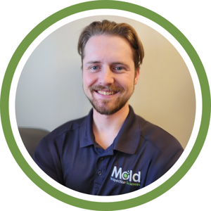 A man with short hair and a mustache, wearing a Mold Inspection Sciences shirt, stands smiling. The image, framed by a green circular border, subtly evokes the precision of testing with its perfect symmetry.