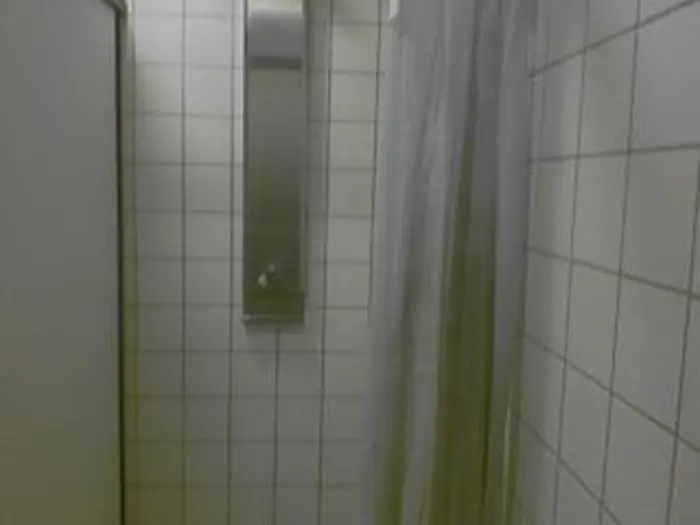 A tiled shower with a stainless steel panel and a gray curtain partially drawn to the side invites investigation. The white tiles create a clean, modern look, while soft lighting casts subtle shadows, enhancing the space's elegant simplicity.
