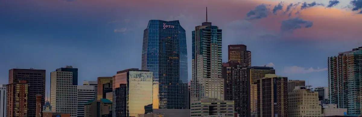 A cityscape featuring a variety of modern skyscrapers against a dramatic sky at sunset invites inspection. The tallest building proudly displays Optiv, while clouds tinged with shades of pink and purple contrast with the dark outlines of the structures below.