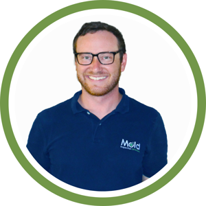 A man with glasses and a beard smiles at the camera, exuding confidence. He wears a navy blue polo shirt proudly displaying the Mold Inspection logo. Framed by a green circular border, he embodies professionalism in mold investigation and inspection.