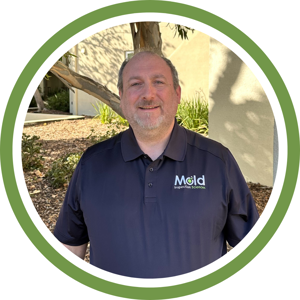 A man in a dark polo shirt with a Mold Inspection Sciences logo stands outdoors, smiling and framed by a circular green border. Trees and a building are visible in the background, reflecting the thorough inspection and testing expertise he represents.