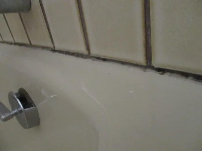 Bathtub with a metal faucet, showing discolored and cracked grout against beige tiles, indicating possible water damage or mold. An inspection is recommended to prevent further deterioration or mildew growth.