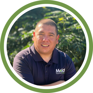 A smiling man in a navy blue polo shirt stands outdoors, framed by trees. The image has a green circular border. The shirt features a logo with the word Mold and the tagline Inspiration Inside, hinting at innovation in testing.