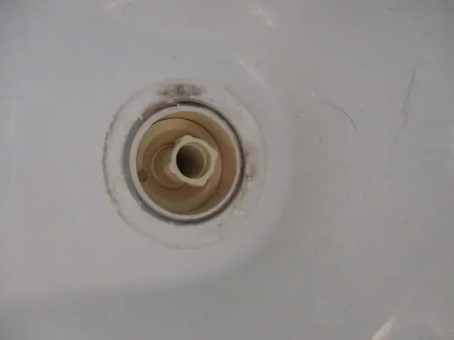 Close-up of a bathtub drain with visible rust and stains around the edges, resembling an investigation scene. The drain cover is missing, revealing a circular opening. The surrounding white surface, ripe for sampling, has scratches and discoloration.