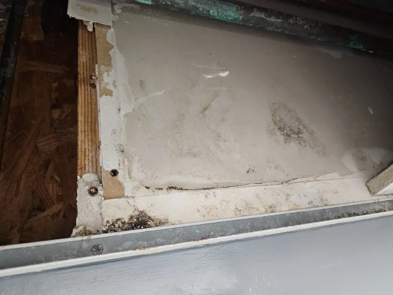 A close-up of a wall or ceiling corner shows water damage and mold growth on drywall, suggesting areas that may require further inspection, with stained and warped surfaces next to exposed wood and metal trim.