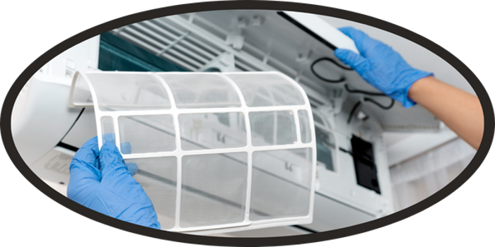 A person wearing blue gloves is inspecting or replacing the mesh filter of an air conditioning unit for mold, with the front panel of the unit open.