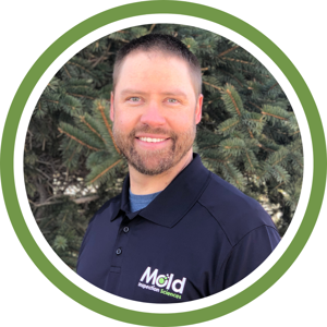 A person with short hair and a beard smiles at the camera, exuding confidence in their mold inspection expertise. They wear a dark polo shirt with a Mold Inspection Sciences logo. The evergreen trees in the background add serenity, while the image is framed by a vibrant green circle.
